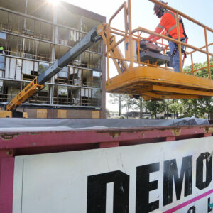 Construction worker using a lift for demolition work on a building, with a visible "DEMO" sign on a container, emphasizing construction and exit strategy marketing.