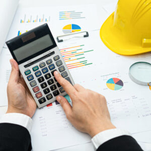 Person using a calculator to analyze financial data, with construction charts and a hard hat in the background, emphasizing revenue strategies for construction companies.