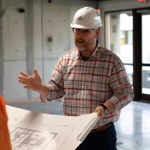 Construction professional in a hard hat discussing blueprints in a building site setting, emphasizing effective construction marketing strategies and client acquisition.