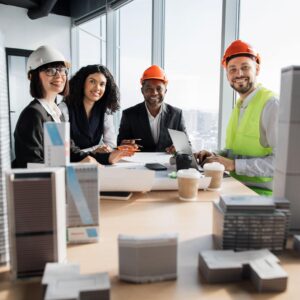 Team of construction professionals collaborating at a table with architectural models and coffee cups, discussing marketing strategies for the construction industry, highlighting the role of fractional CMOs.