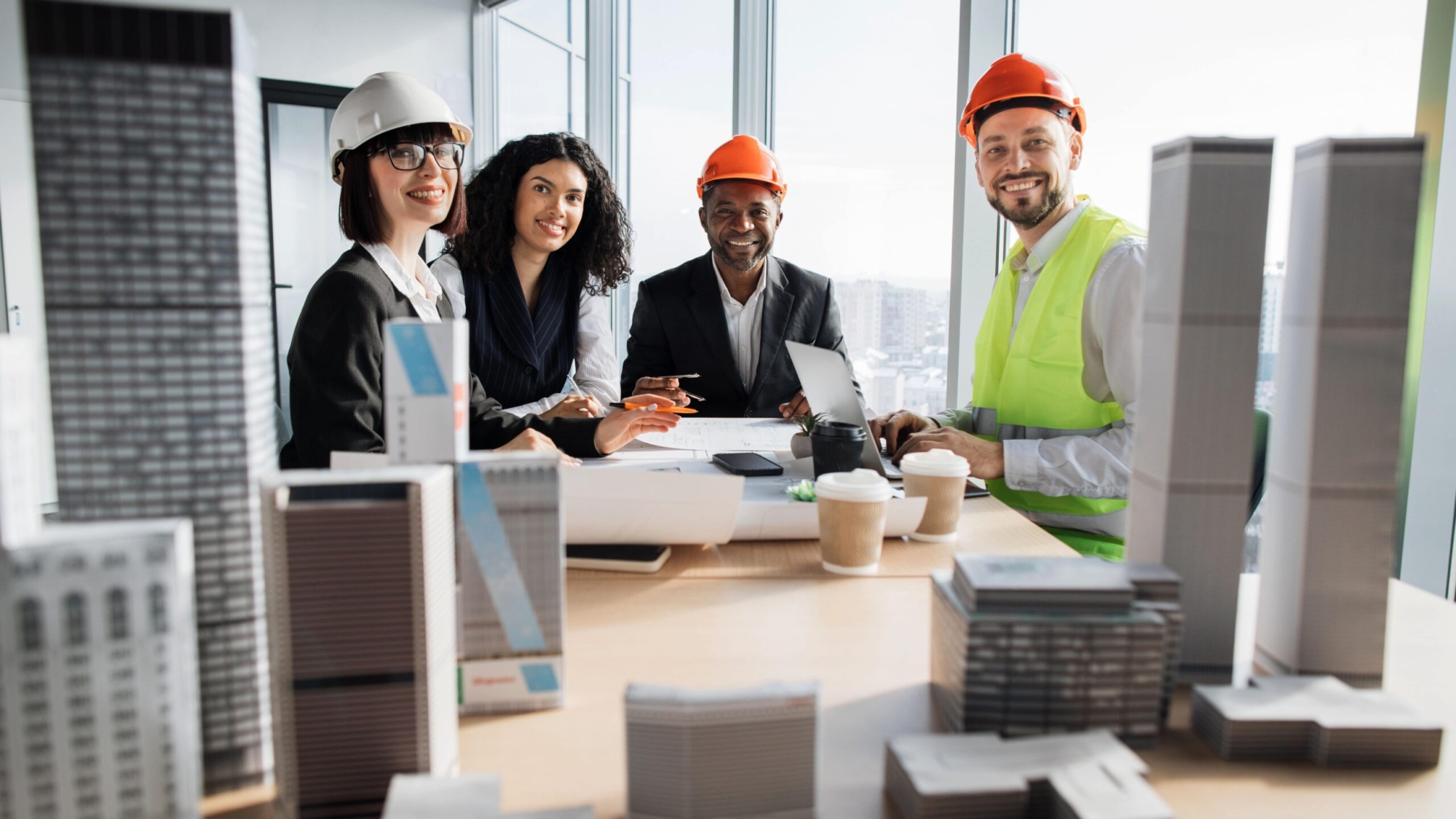 Diverse team of construction professionals collaborating at a table with building models, discussing marketing strategies, and planning projects.
