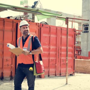 Construction manager holding plans and clipboard on job site with orange containers in background, illustrating StoryBrand principles for construction companies.